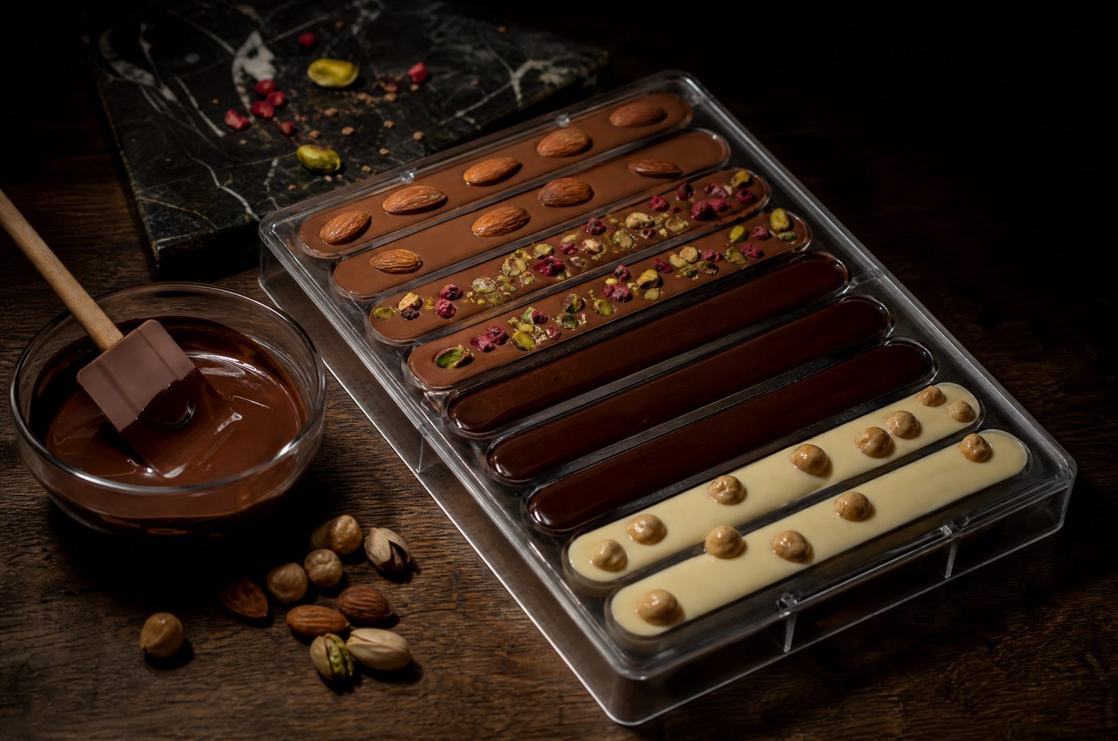 A bar mold freshly filled with chocolate and a bowl of coating